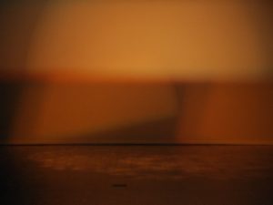 an orange image of a stage, the stage lighting depicts swinging orange lights, the stage floor is scattered with orange spots