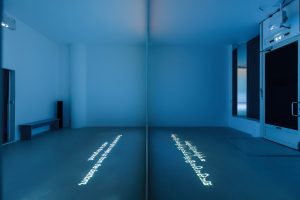 a room lit blue by the projected image in the middle, with the English text on the left, and the Tibetan text on the right.