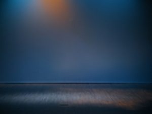 a stage depicting blue light and orange spot in the background, with white light on the stage floor