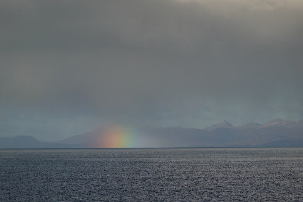 rainbow light seen as a short brush stroke on the horizon where ocean meets mountains