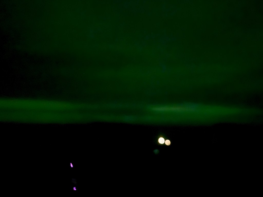 a textured green aurora light in the village with house lights on
